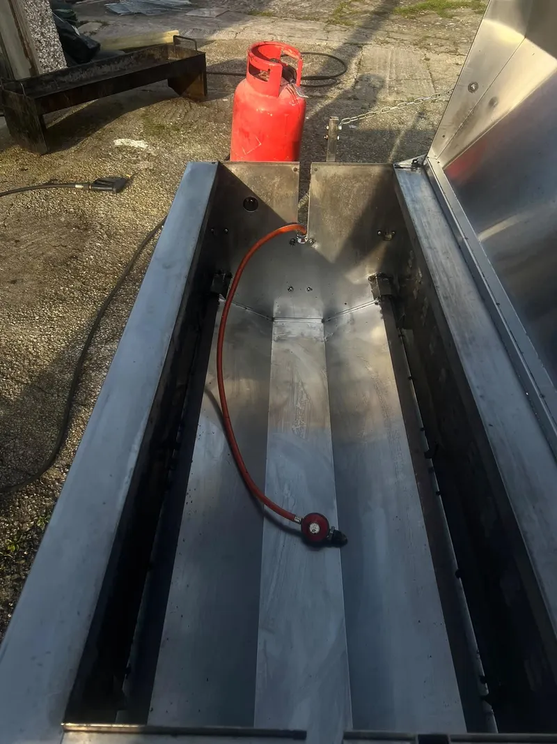 Inside a hog roast machine after cleaning, with its gas hose and burner